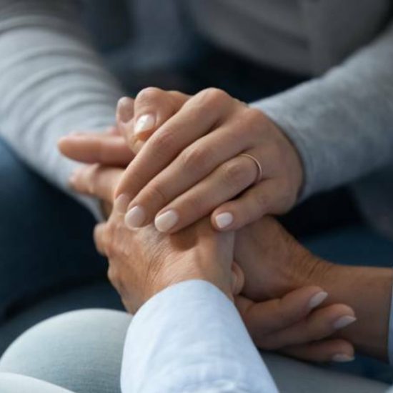 A close up of a younger lady holding the hands of an elderly lady in a supportive way