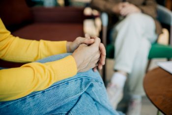 Close-up of an unrecognizable woman's hands crossed on her knee, client at a session with a psychologist.