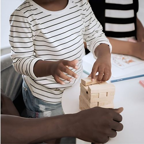 A close up of a dad building jenga blocks with his toddler son
