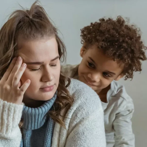 Stressed out mum holding hear head with mischevious son looking over her shoulder